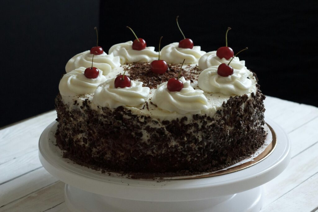Delicious Black Forest cake topped with whipped cream and cherries on a cake stand.