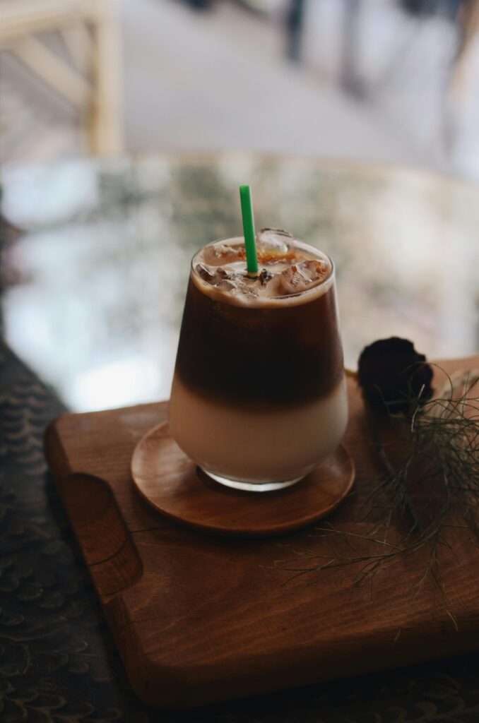 A creamy iced coffee served with a straw on a wooden tray, capturing a cozy cafe ambiance.