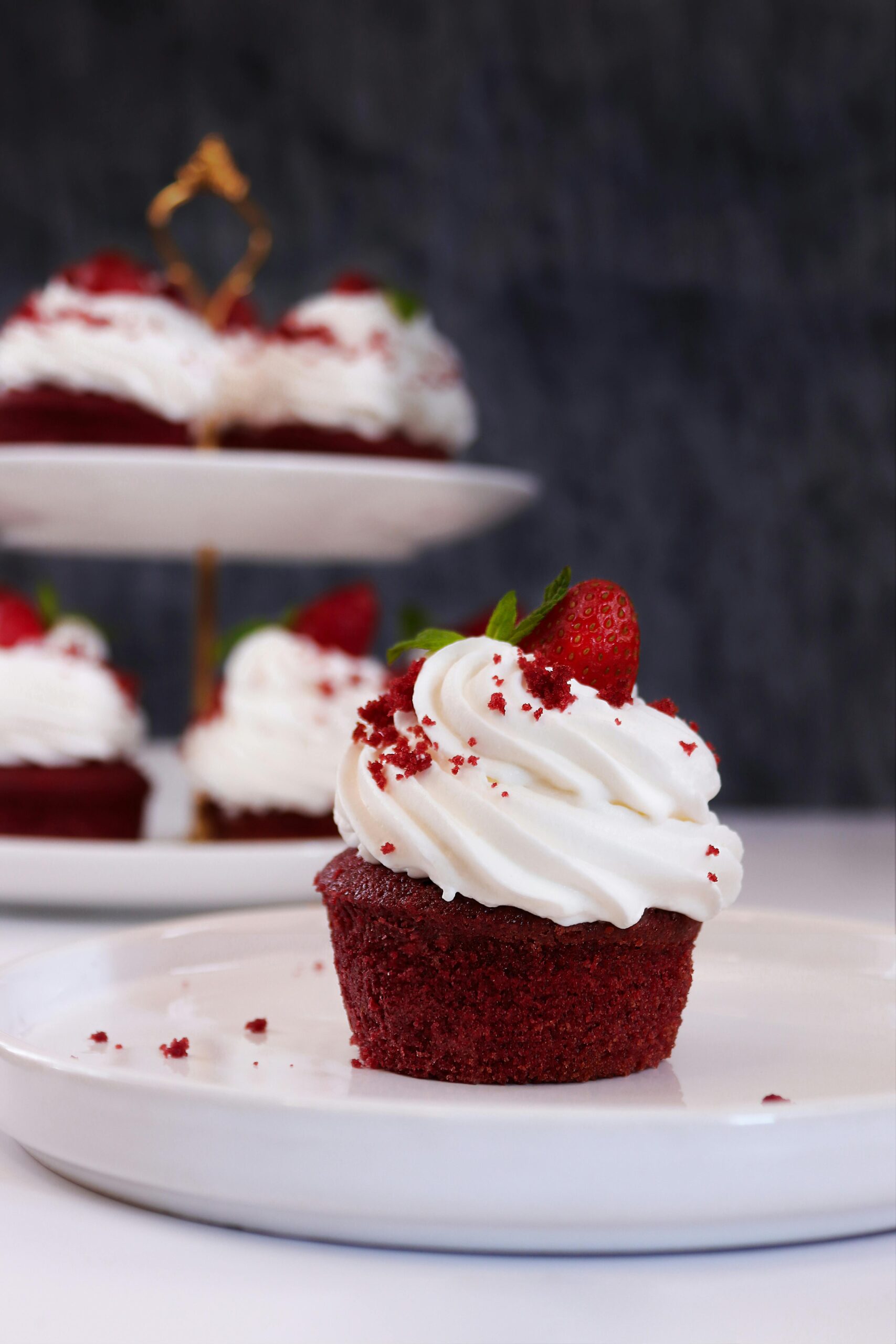 A tempting red velvet cupcake topped with creamy frosting and strawberry on a white plate.