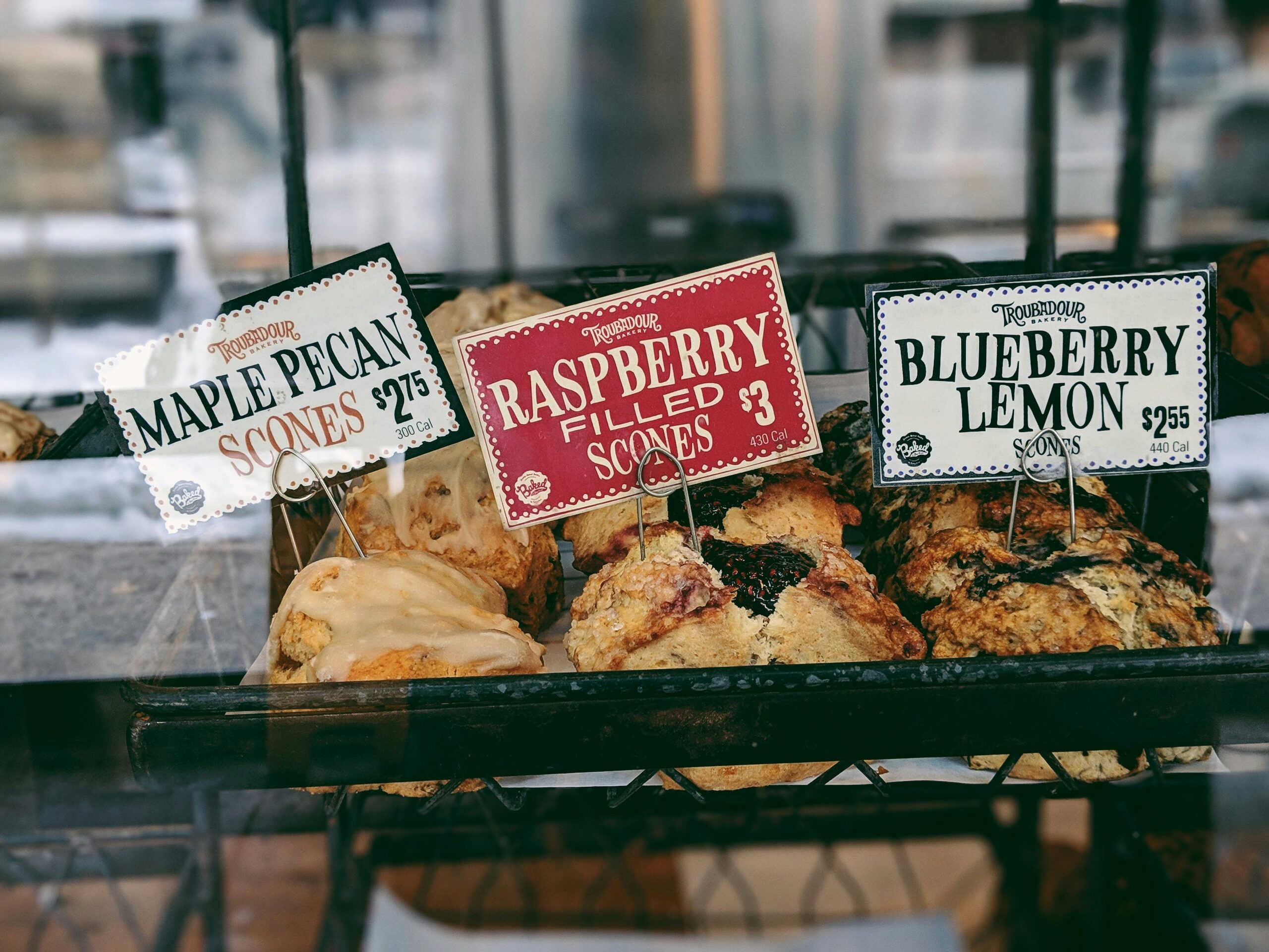 A selection of maple pecan, raspberry, and blueberry lemon scones on display in a bakery.