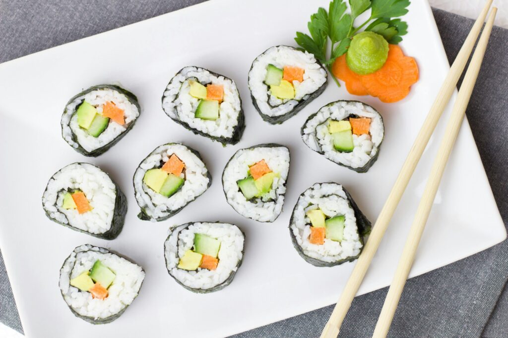 Top view of vegetable sushi rolls with chopsticks and wasabi on a white plate.