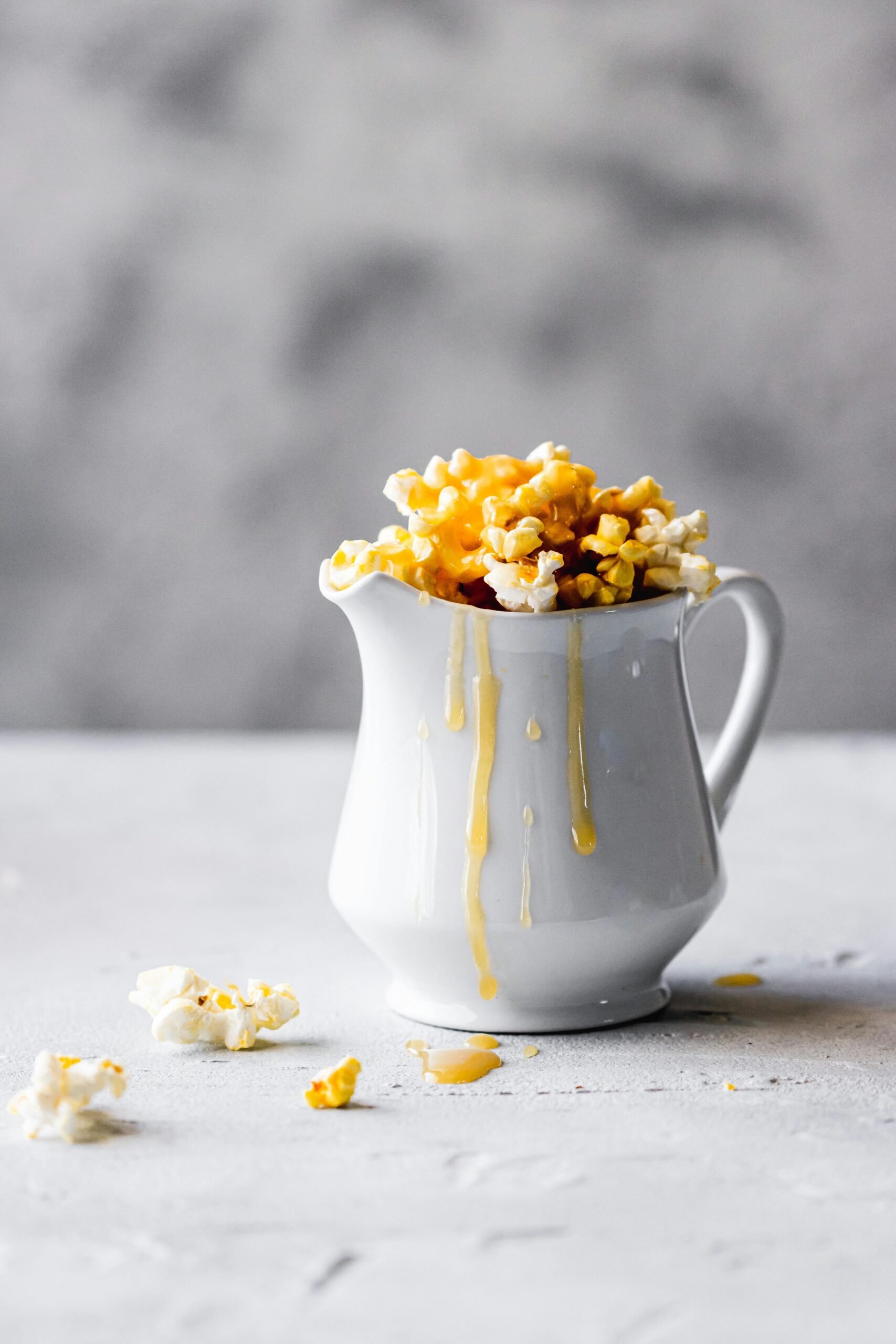 Delicious caramel popcorn spilling from a white jug, artistic food display.