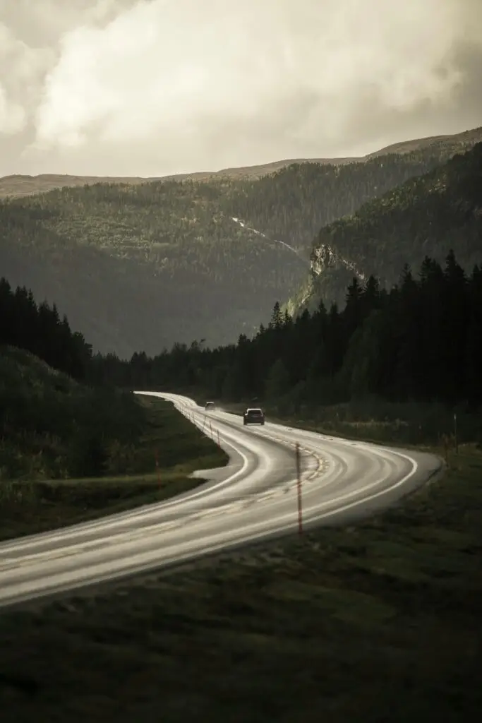 Winding road leading through lush mountains in Norway under a soft sky.