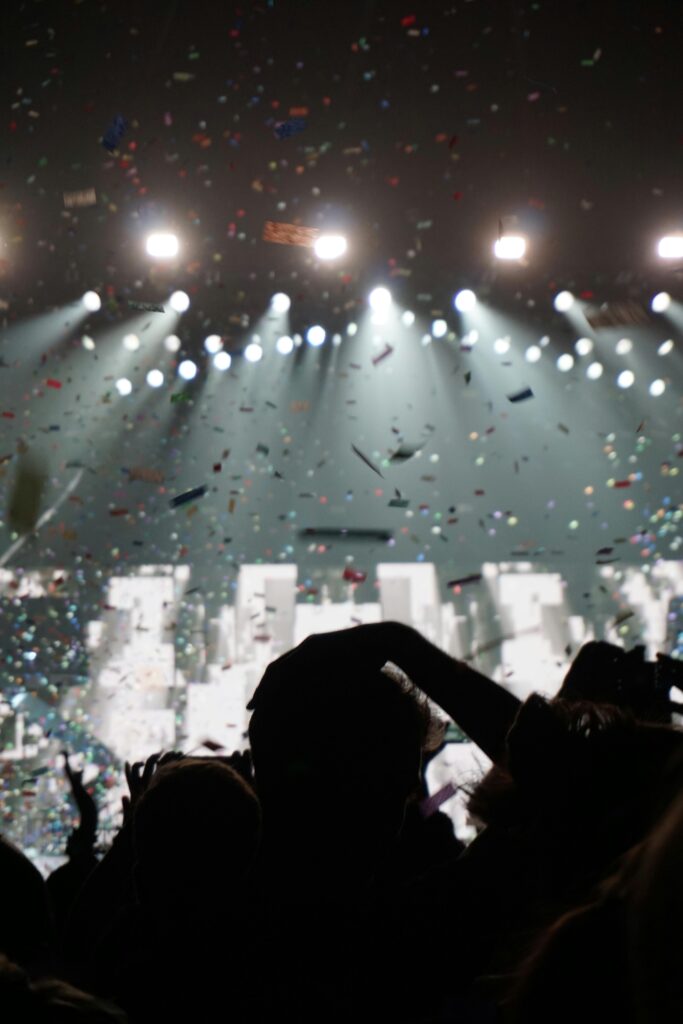 Silhouetted crowd enjoying a concert with vibrant confetti and bright stage lights.