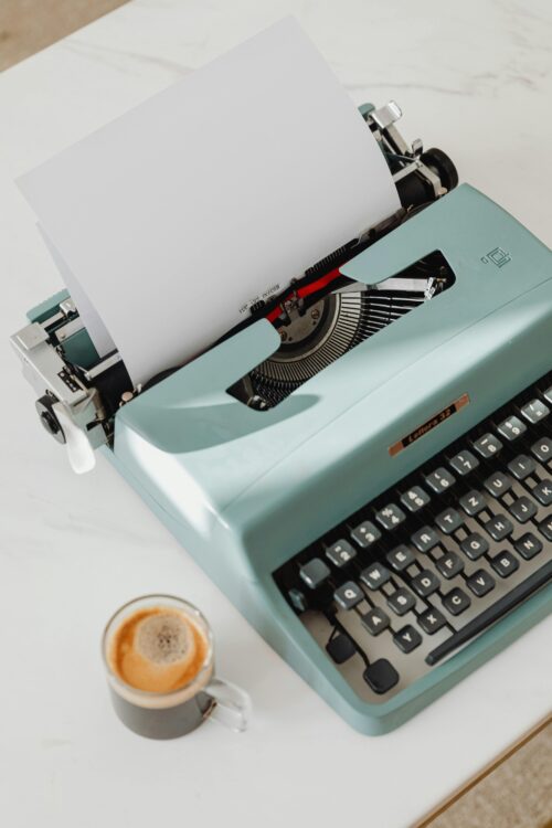 A retro typewriter and a cup of coffee on a white table, evoking vintage vibes.