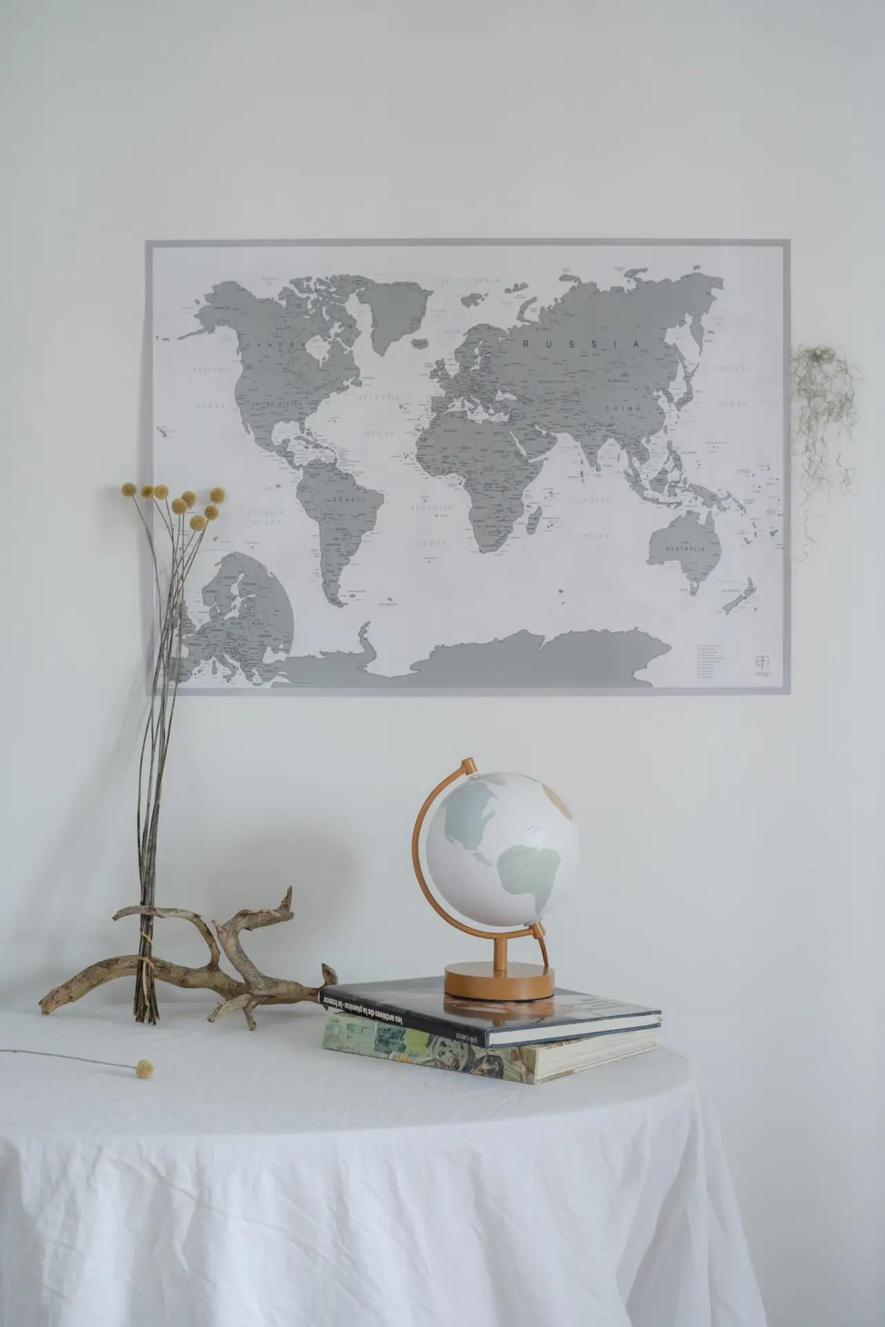 A minimalist decor featuring a world map, globe, books, and dried flowers on a table.