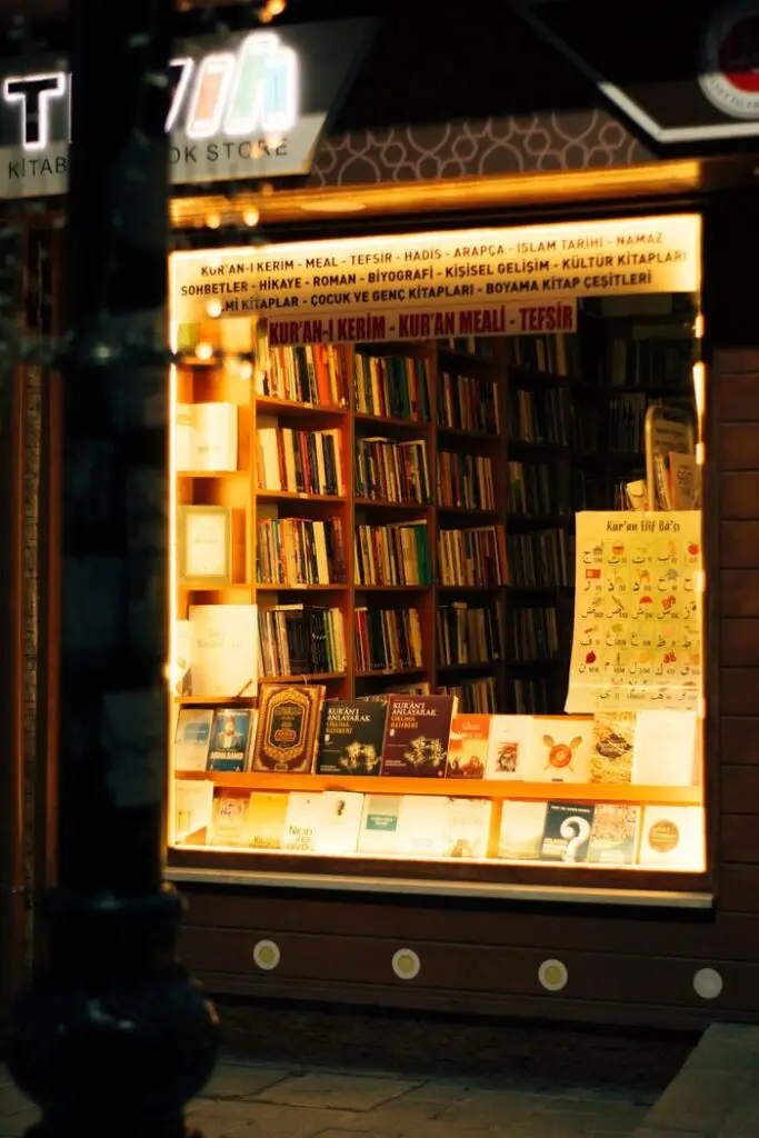 Warmly lit bookstore window displaying a variety of books at night.