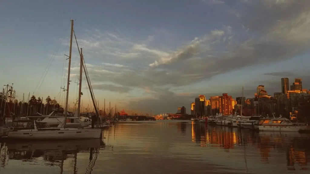 A stunning view of boats docked at a marina during golden hour, with the Vancouver skyline bathed in warm sunset light.
