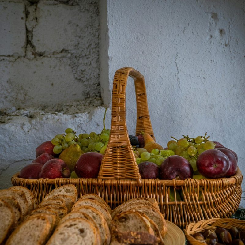 A rustic setting with fresh bread loaves and a wicker basket filled with grapes and plums.