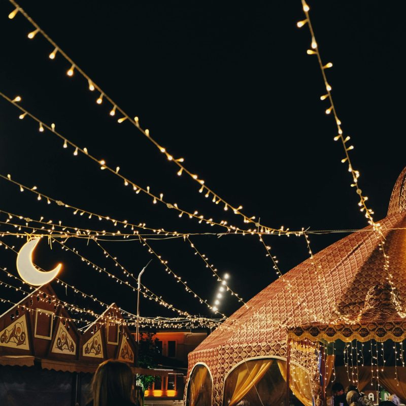 A lively night festival scene with decorative tents and string lights creating a festive atmosphere.