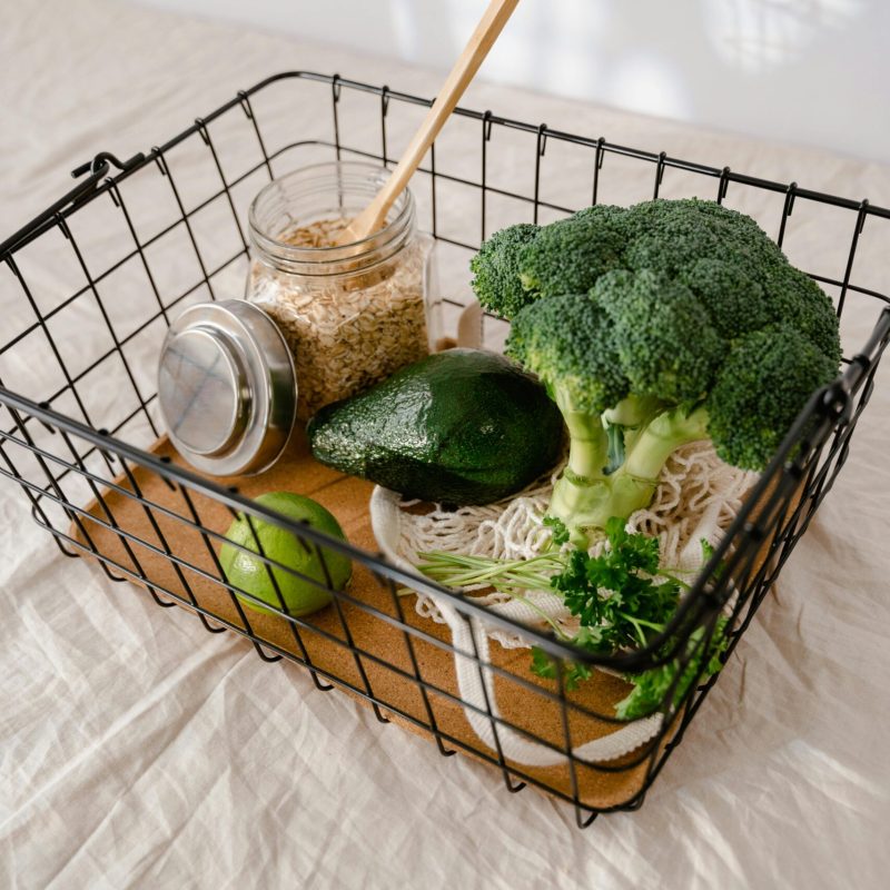 Fresh broccoli, avocado, and oats ready for healthy meal preparations in a wire basket.